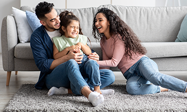 A smiling family sitting on a rug cleaned with OxiClean™ Versatile Stain Remover powder.