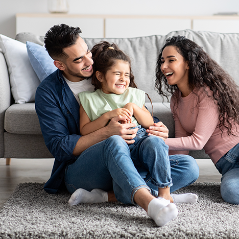 A smiling family sitting on a rug cleaned with OxiClean™ Versatile Stain Remover powder.