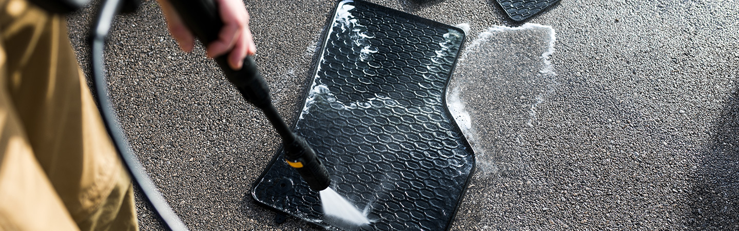 Person spraying rubber car mats with pressure washer.