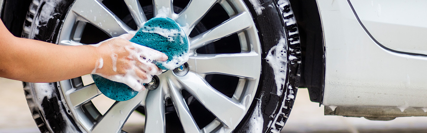 Person cleaning car tires with sponge.
