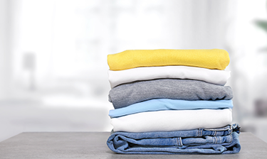 Folded pile of colored and white clothing after being cleaned with oxygen bleach.