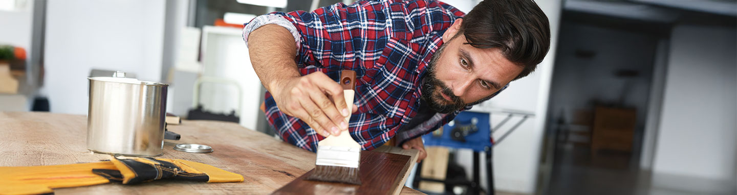 Man in striped flannel painting a wood panel.