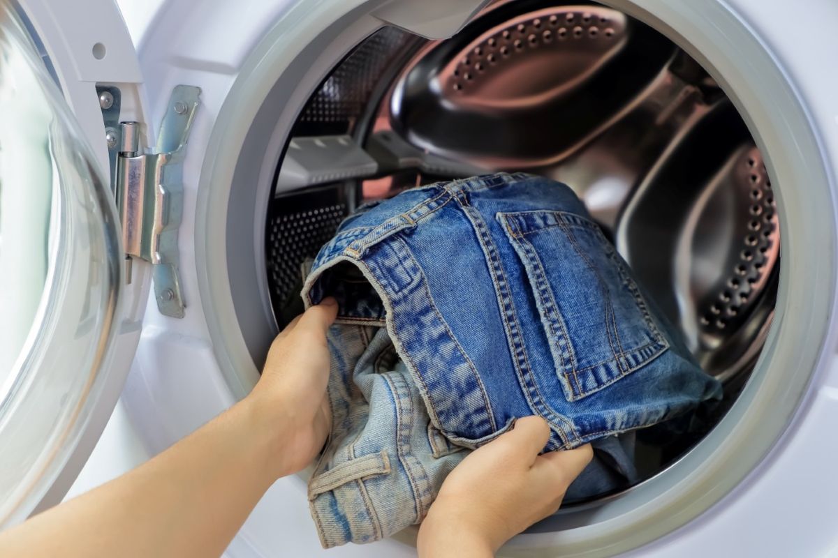 A person putting two pairs of jeans in a front-load washing machine.
