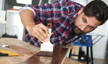 Man in striped flannel painting a wood panel.