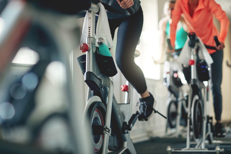 Close-up of athletes’ legs pedaling exercise bikes during a cardio spinning class in a gym.