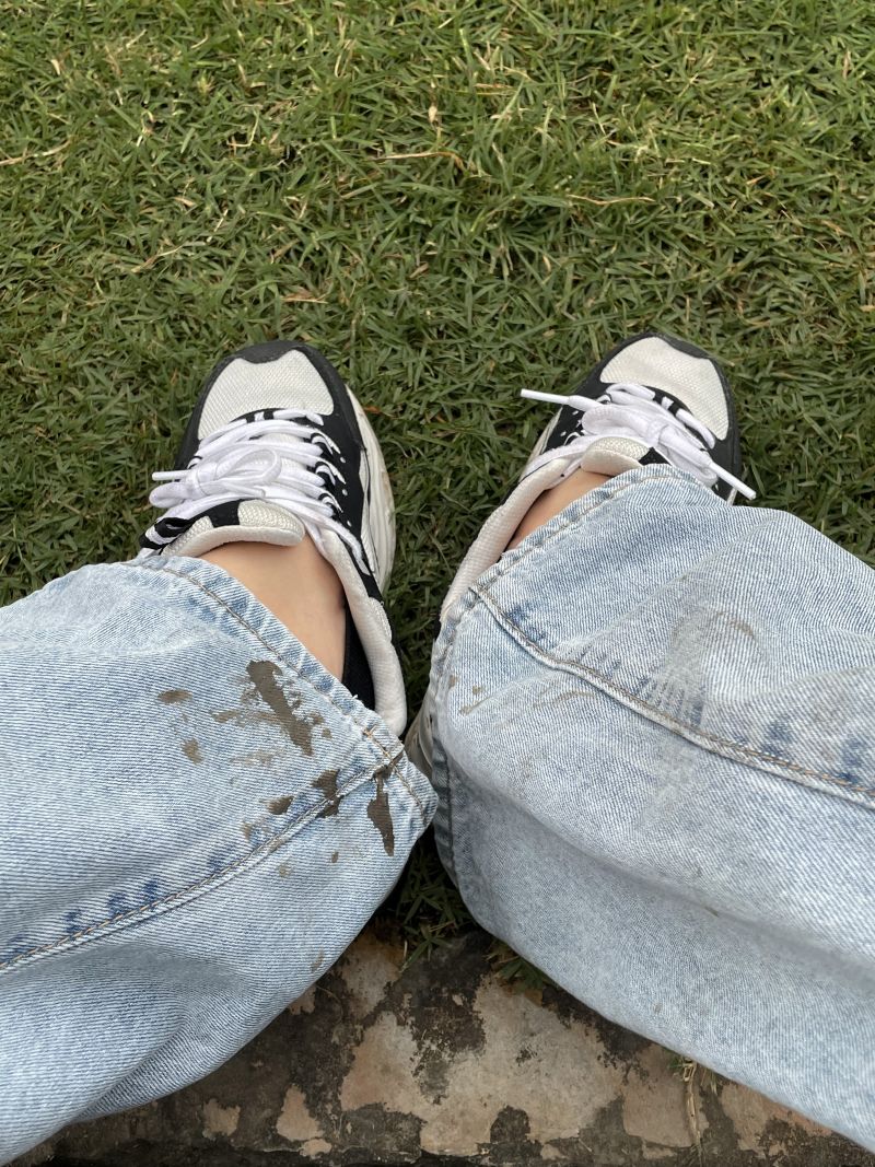 Close-up of muddy jean bottoms and sneakers after outdoor activity.